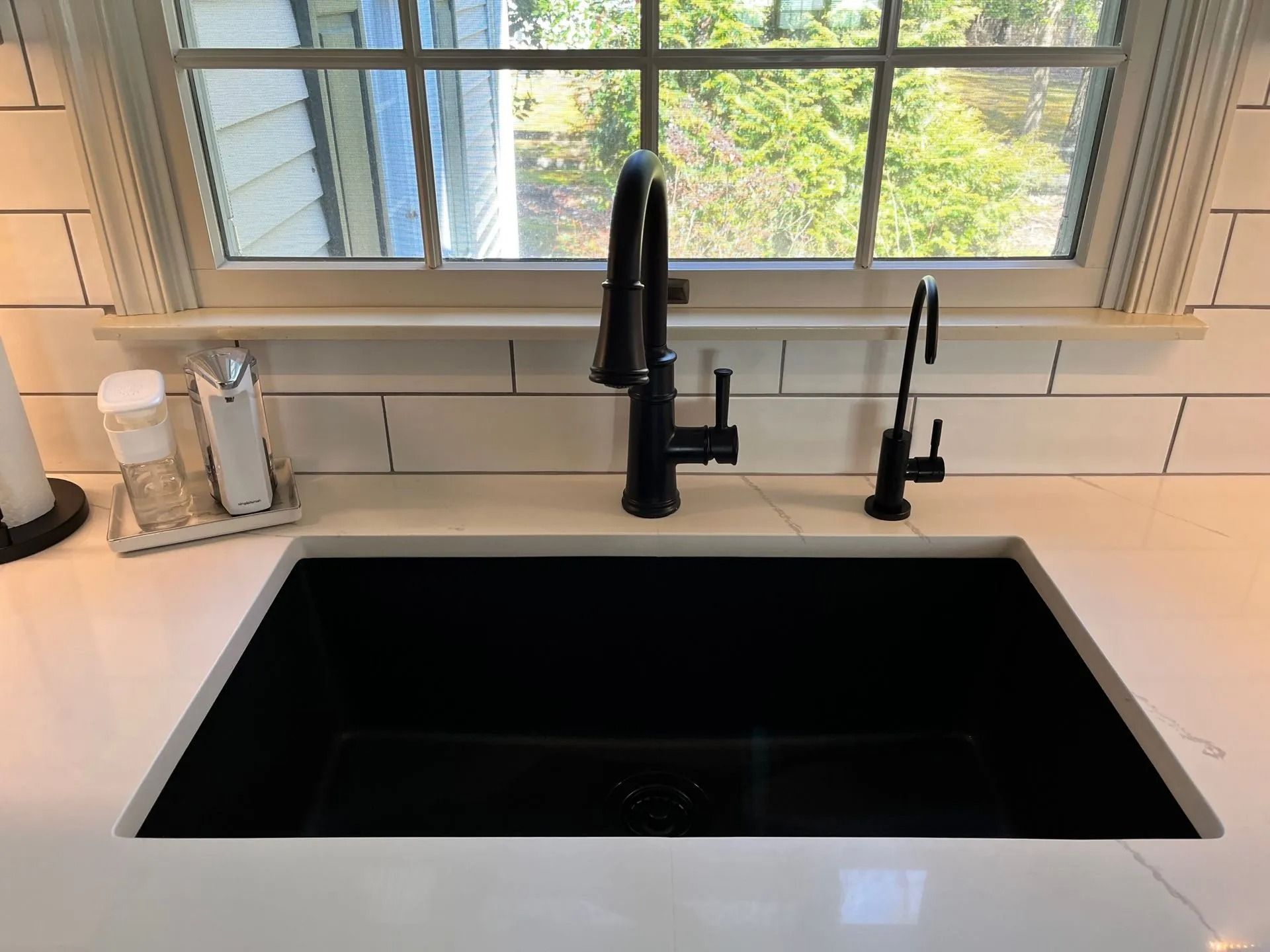 Black sink with matte black faucet beneath a window in a bright kitchen