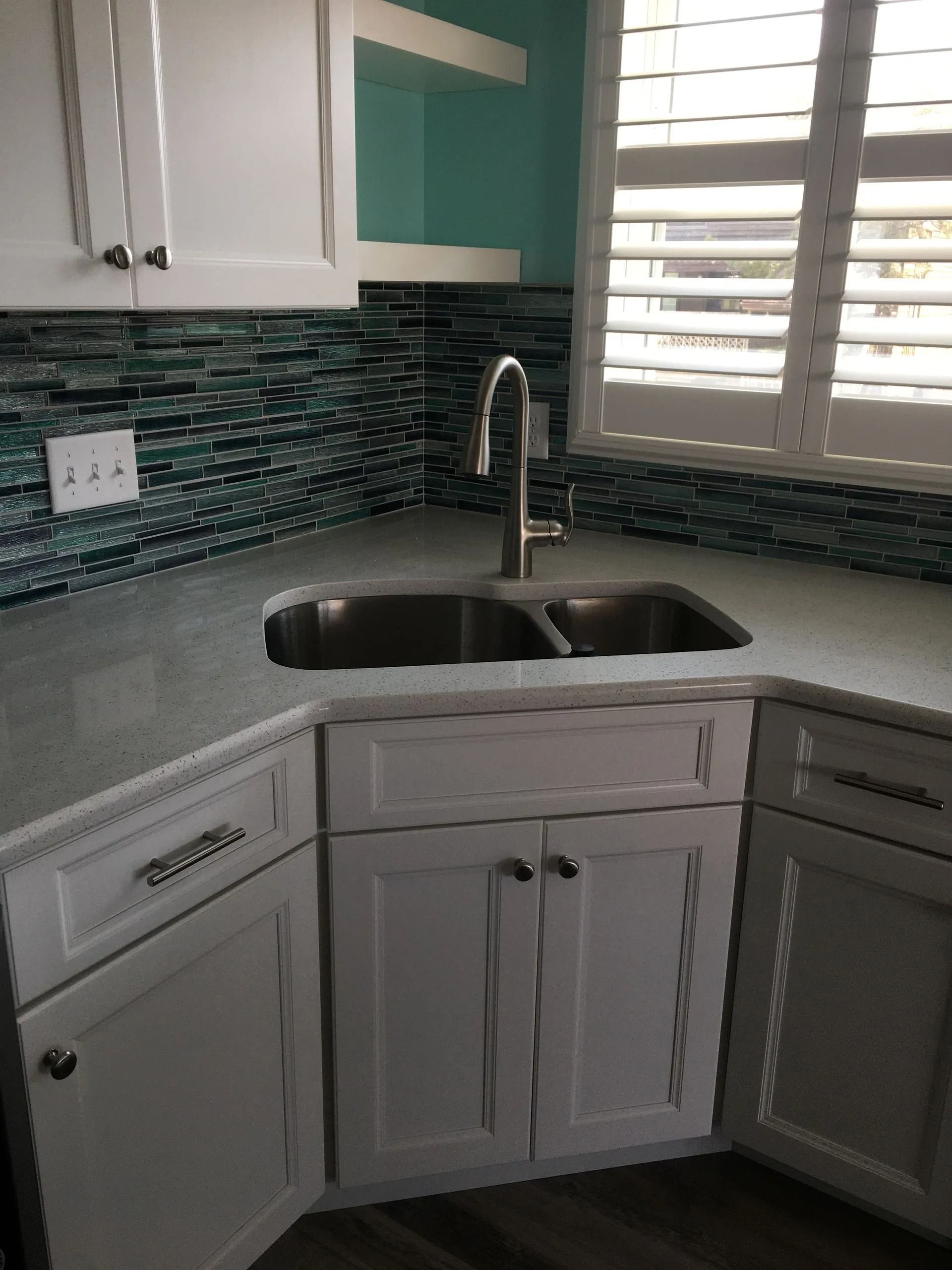 Bright white kitchen corner with teal backsplash, granite countertop, sink, and window shutters