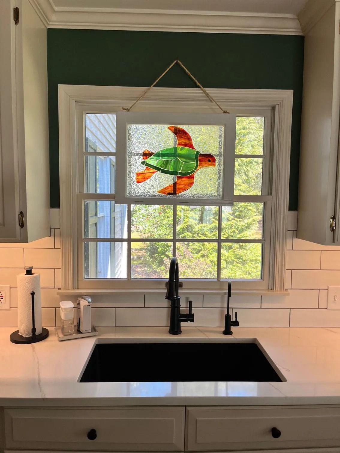 Kitchen sink beneath window with colorful fish stained-glass panel and green walls
