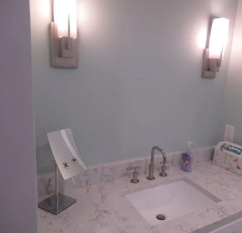Bathroom vanity with white countertop sink, wall sconces, and toiletries beside a mirror.