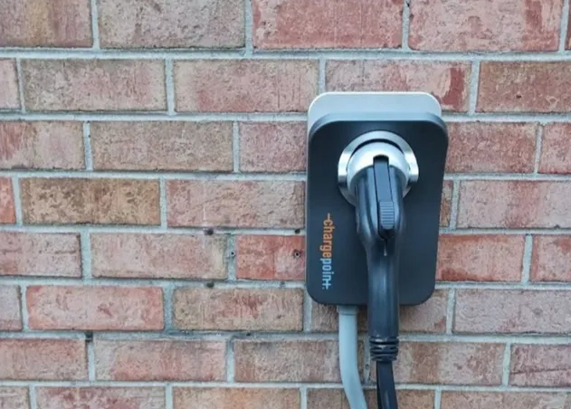 Electric vehicle charging station mounted on a brick wall with coiled cable hanging below