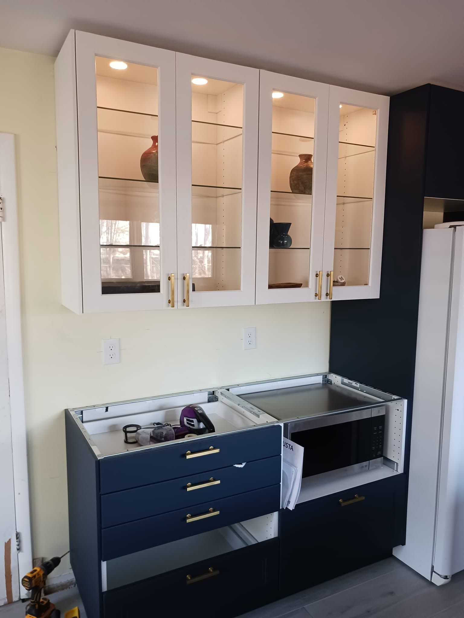 Kitchen cabinets above open drawers and shelves during a renovation, with white doors and dark lower cabinetry.
