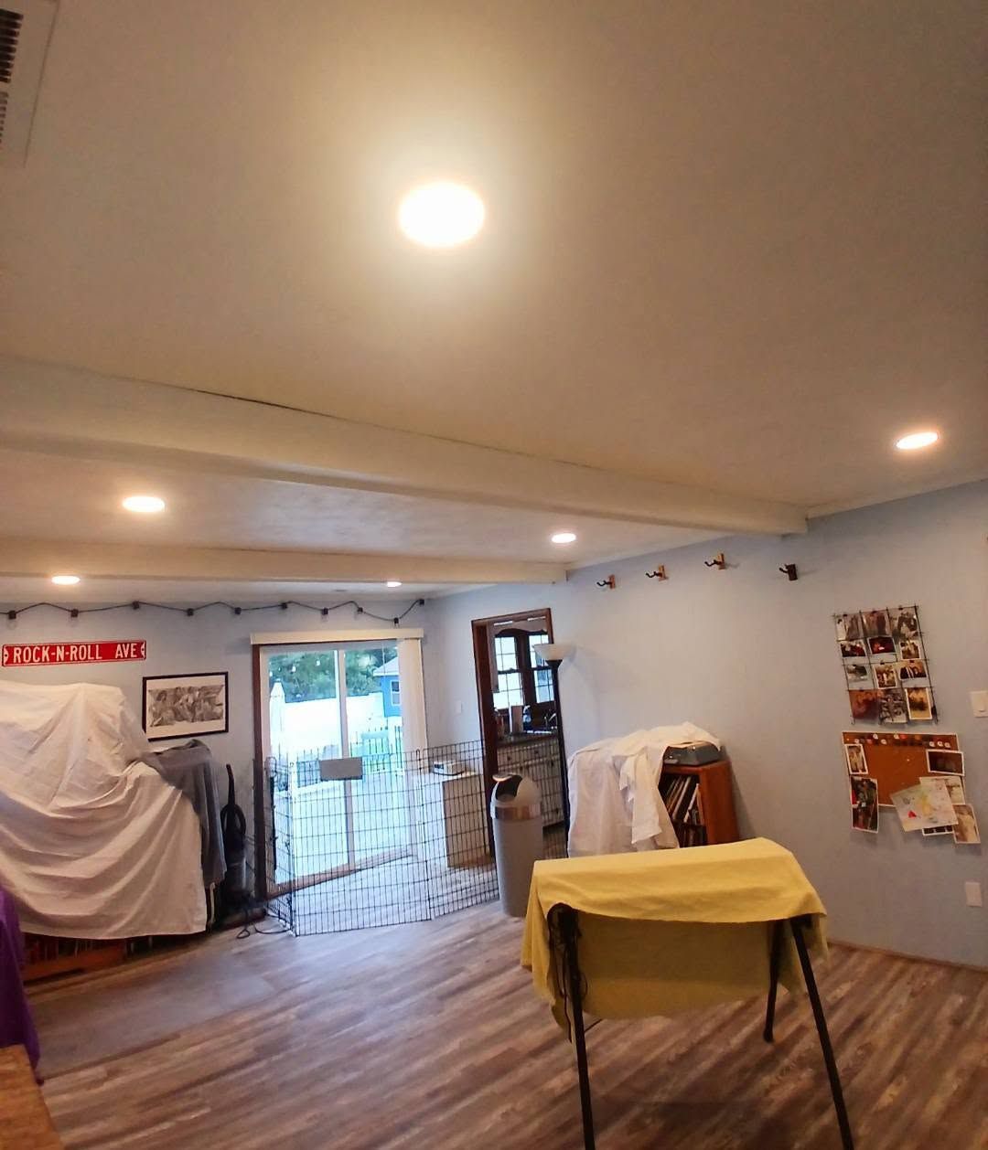 Spacious room with wood floors, ceiling lights, covered items, and an open door to a patio