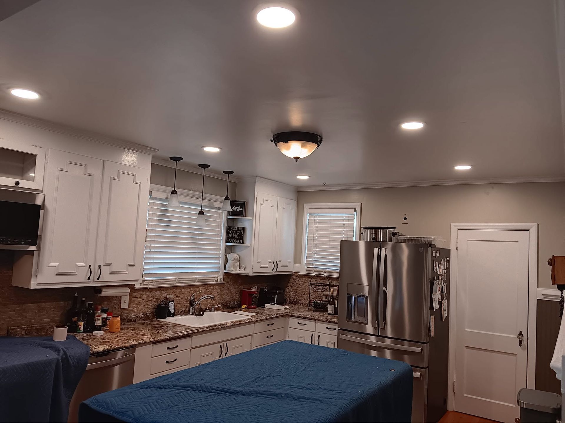 Bright kitchen with white cabinets, stainless fridge, blue island bench, and recessed ceiling lights