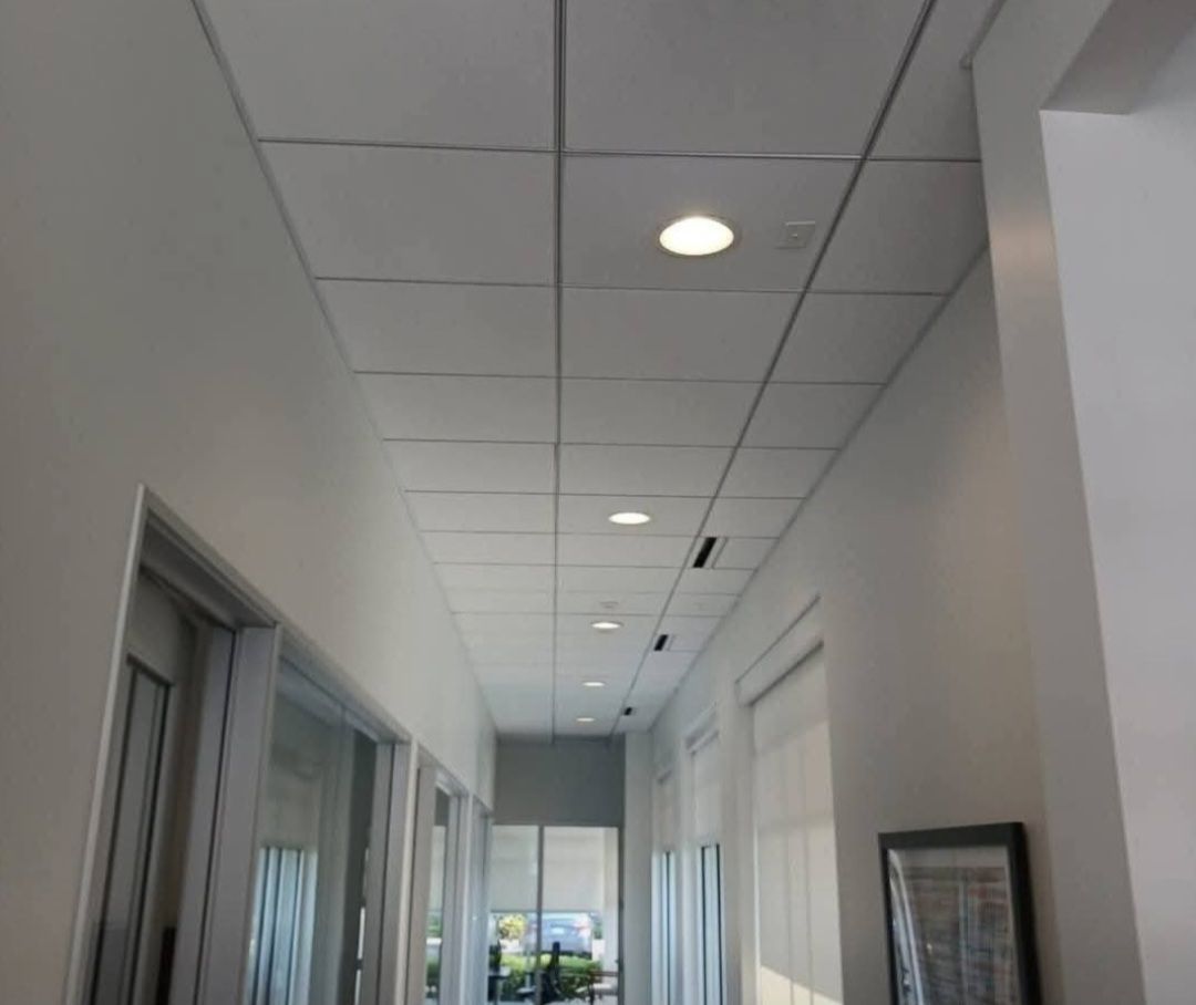 Long office hallway with white walls, ceiling lights, and windows along the left side