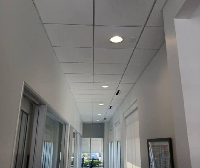 Long office hallway with white walls, ceiling lights, and windows along the left side