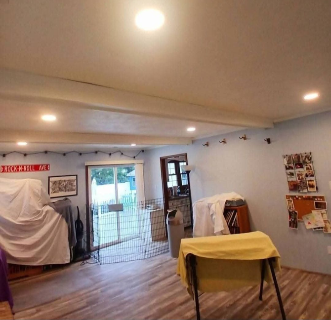 Spacious room with wood floor, ceiling lights, covered furniture, and a table draped in yellow cloth by the window