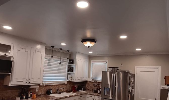 Bright modern kitchen with white cabinets, recessed lights, stainless steel fridge, and window blinds