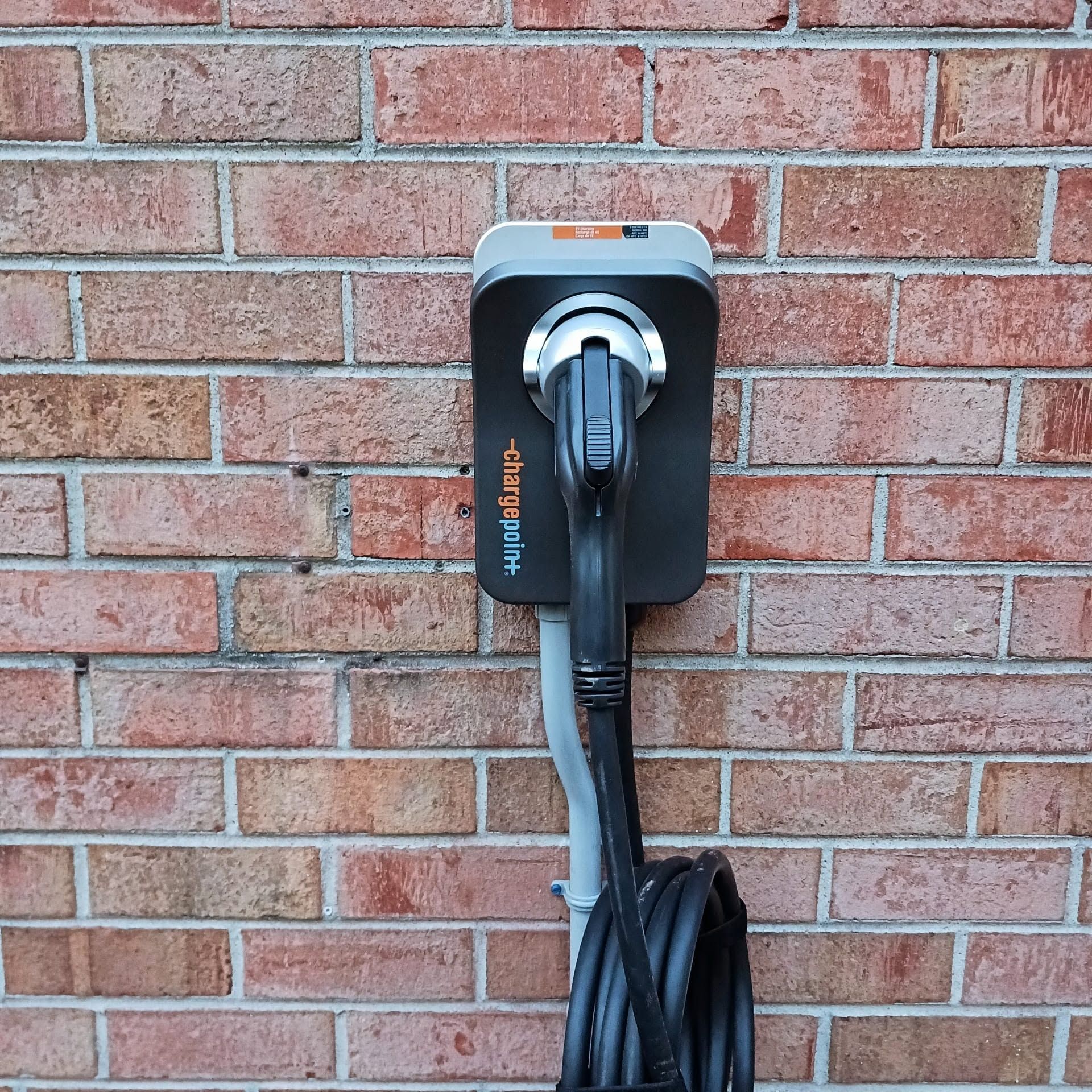 Wall-mounted electric vehicle charging station with a coiled cable on a brick wall.