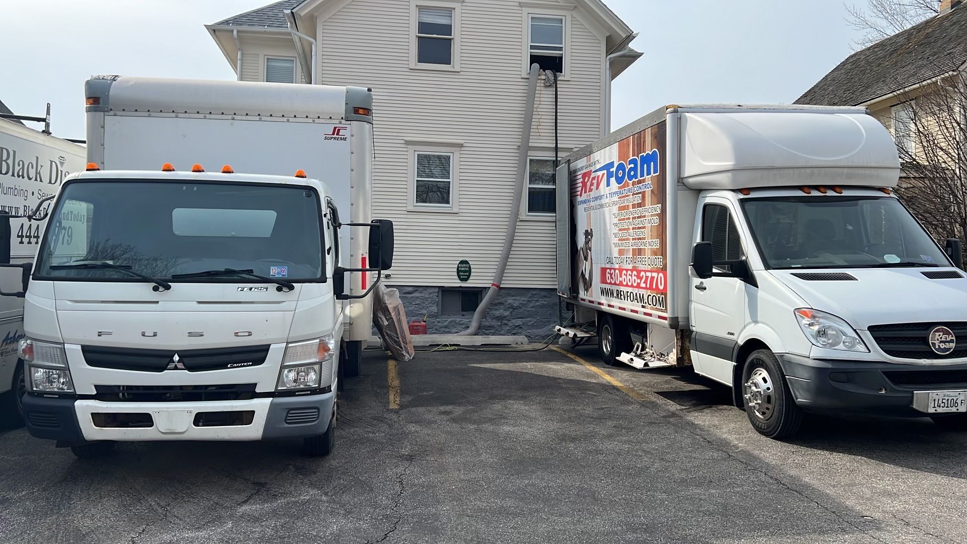 Two white moving trucks parked in a driveway in front of a house, one with its side cargo door open.