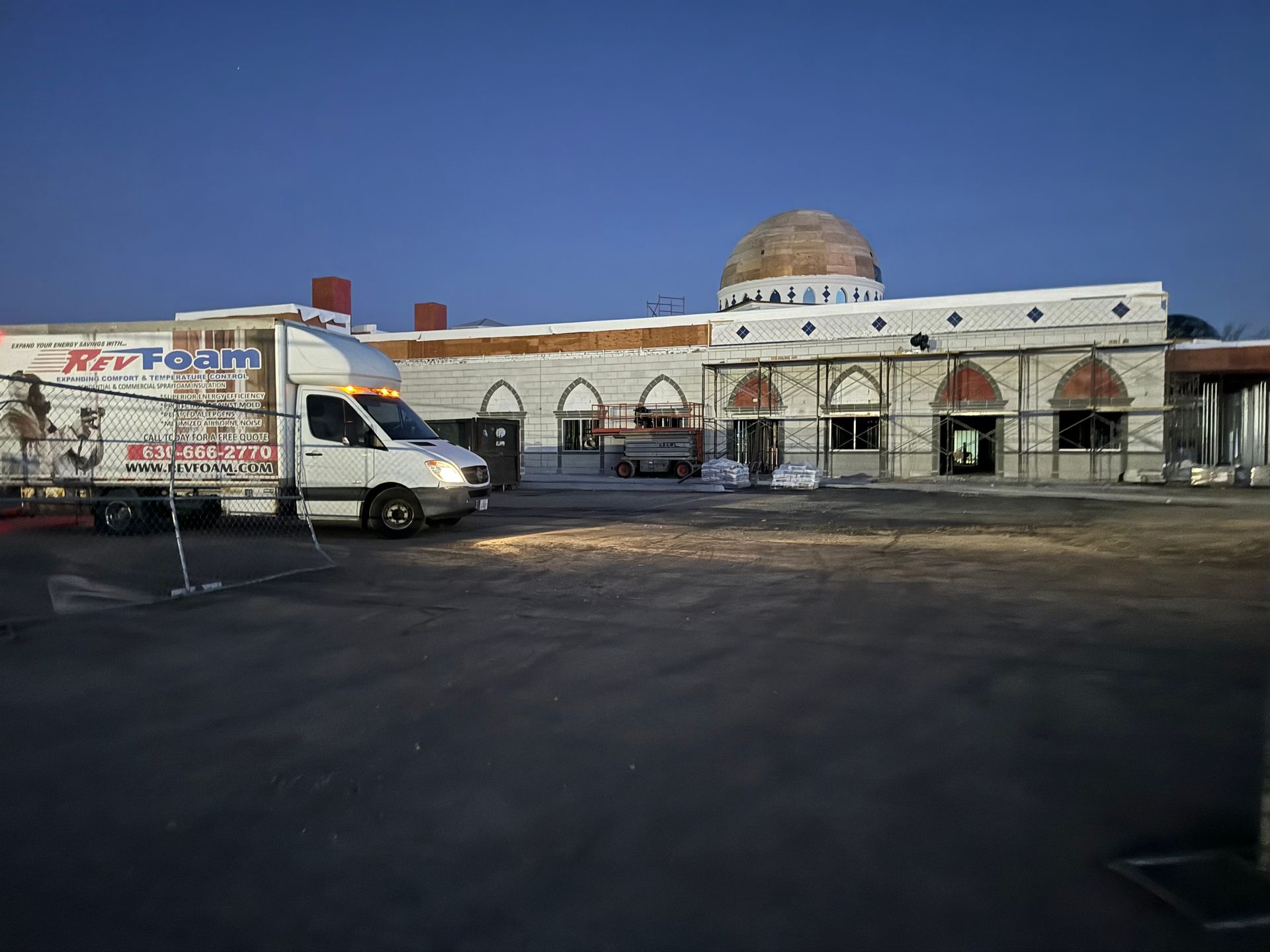 White van parked outside a low building with a dome under a clear blue sky, in a mostly empty lot