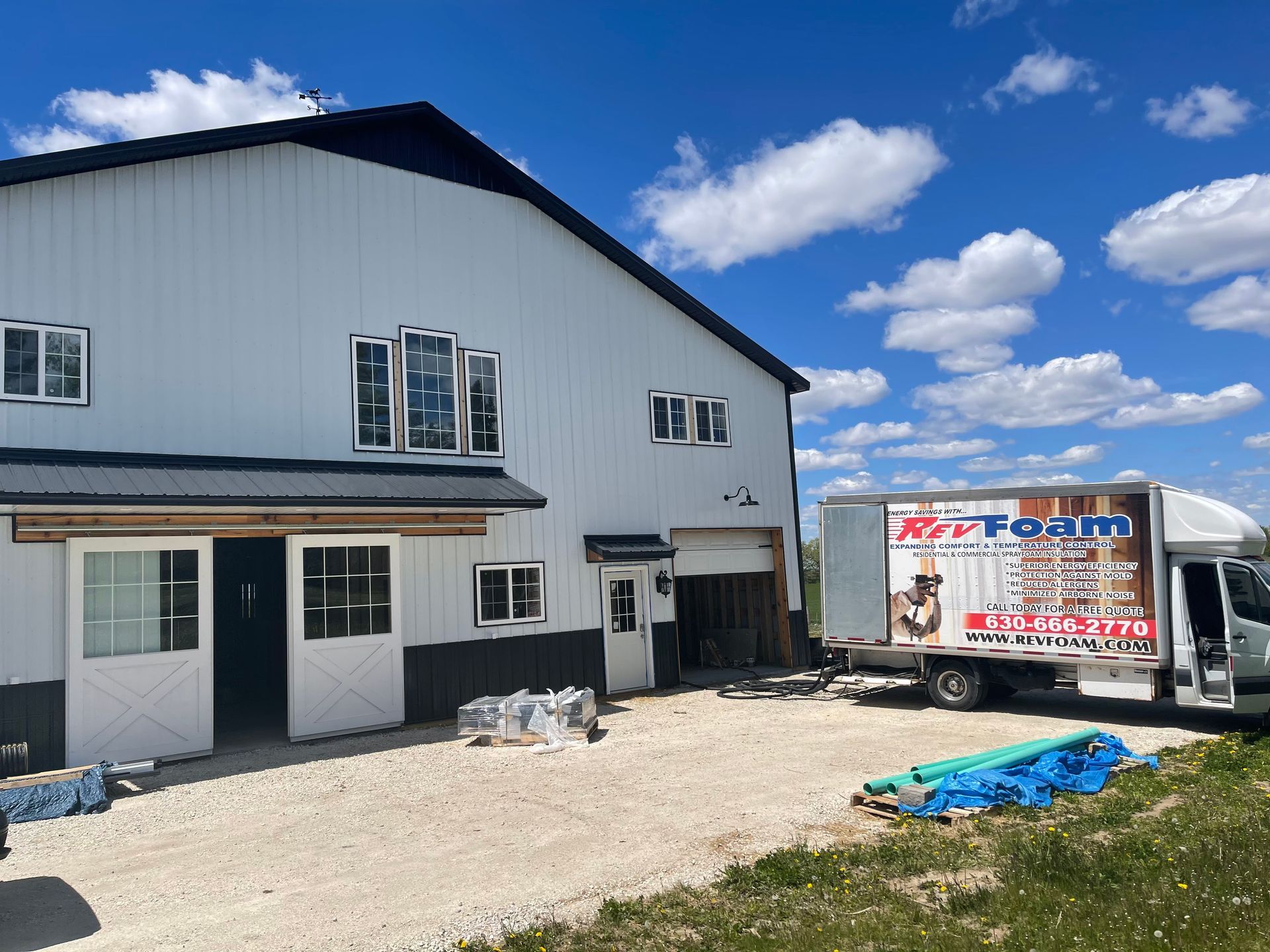White two-story building with a trailer in a gravel lot under a bright blue sky with clouds