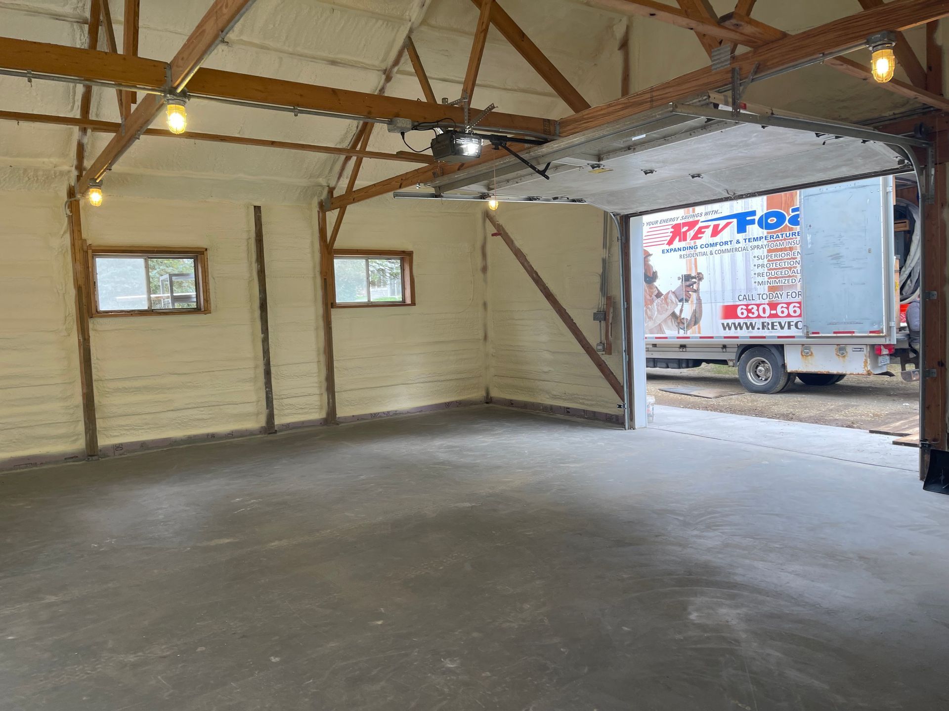 Empty garage with concrete floor, exposed rafters, small windows, and a box truck visible through the open door