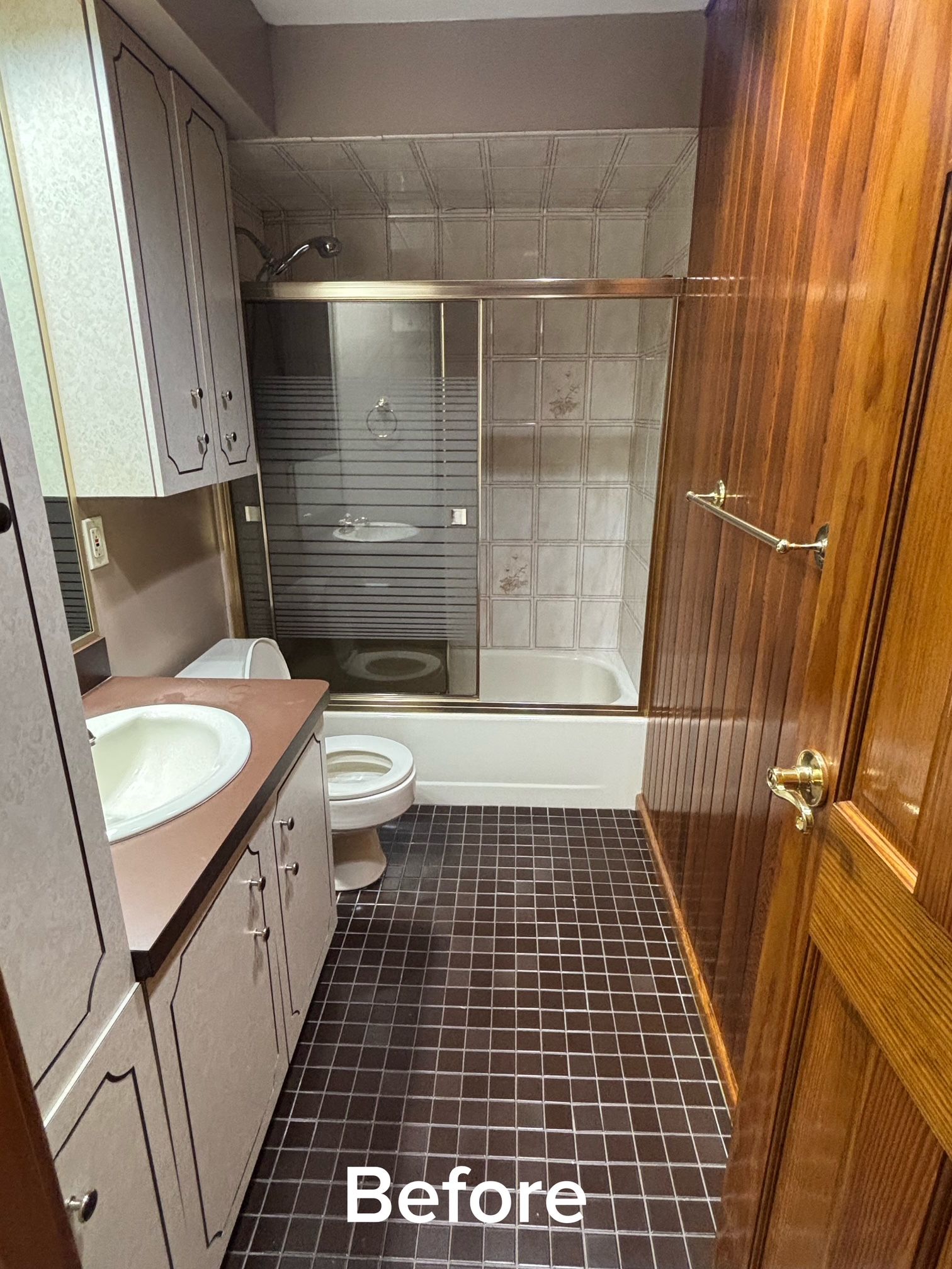 Before photo of a narrow bathroom with brown tile, a sink vanity, toilet, tub, and shower
