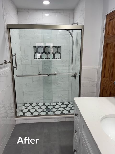 Bathroom shower with clear glass doors, white tile, and black-and-white mosaic accents.