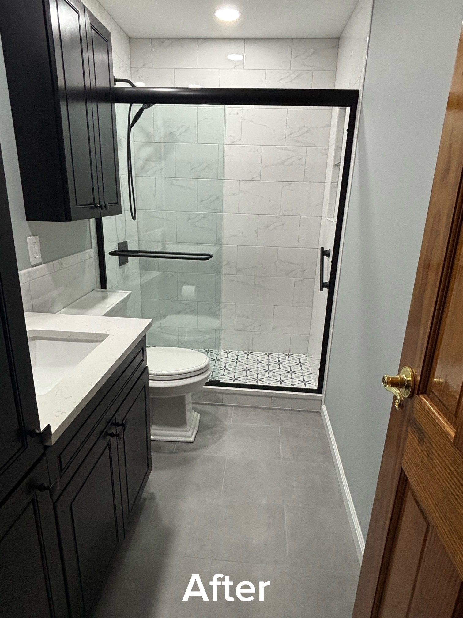 Modern bathroom shower area with black-framed glass enclosure, white tile, dark vanity, and toilet visible.