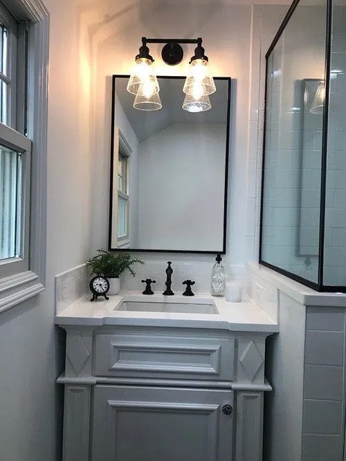 Bathroom vanity with a black-framed mirror, two sconces, white countertop, and gray cabinet.