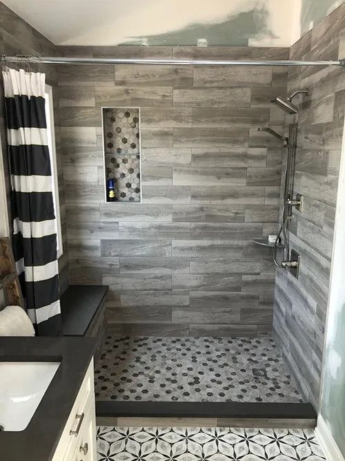 Bathroom with gray and wood-look tile shower. Black and white striped curtain, pebble floor, built-in bench.