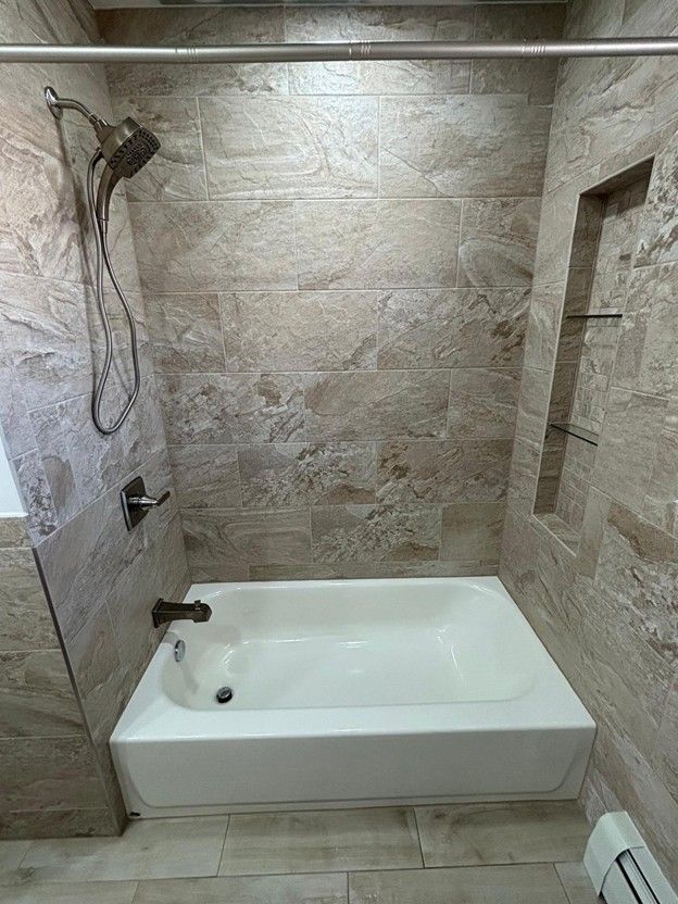 Bathroom with a white bathtub and beige tiled walls; a shower head and storage niche.