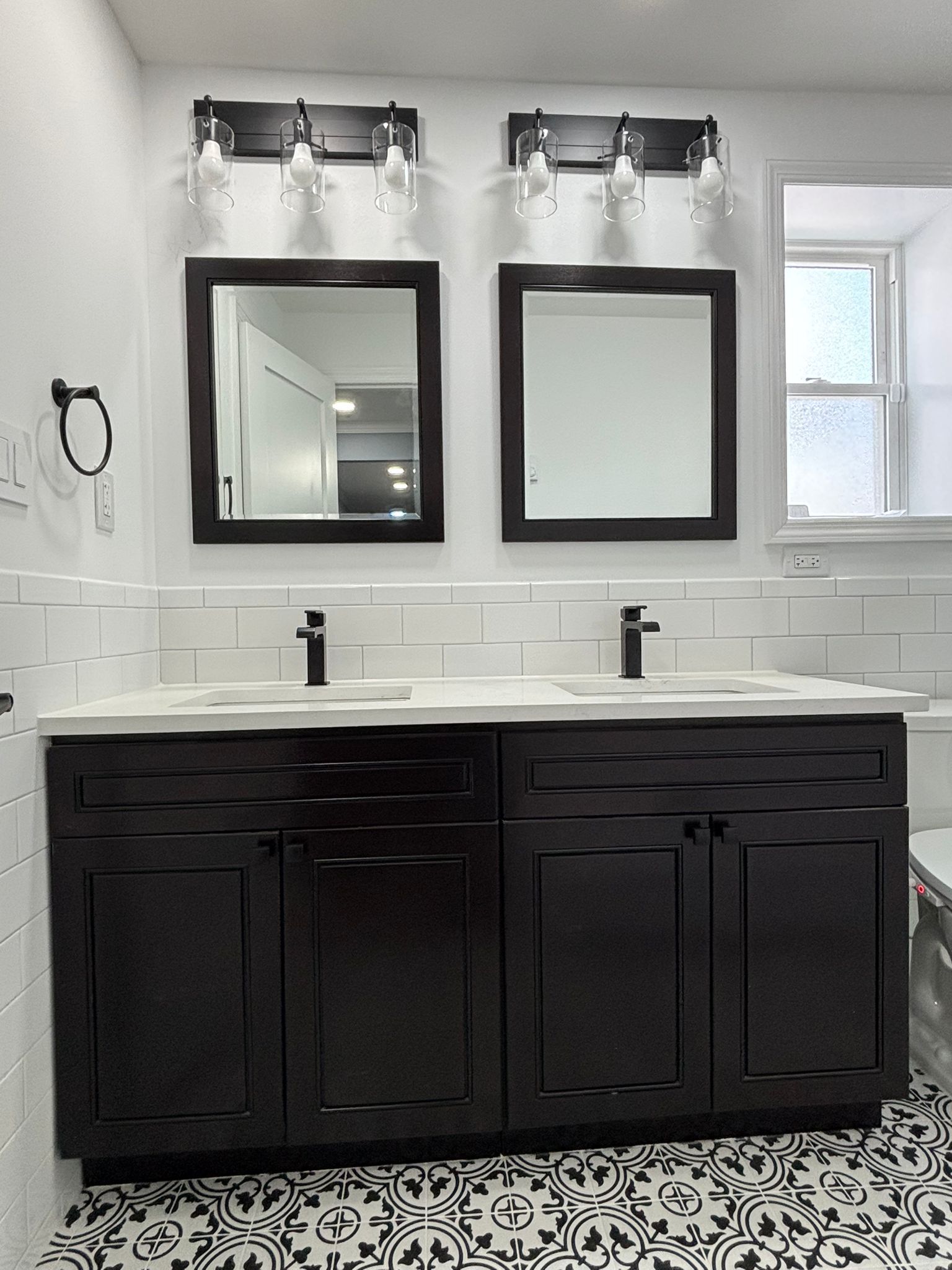 Black and white bathroom with double vanity, square mirrors, and patterned floor.