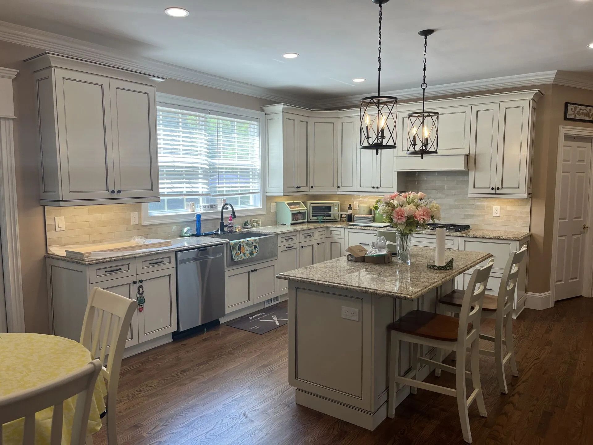 Kitchen with white cabinets, stainless steel appliances, and a granite island with two pendant lights overhead.