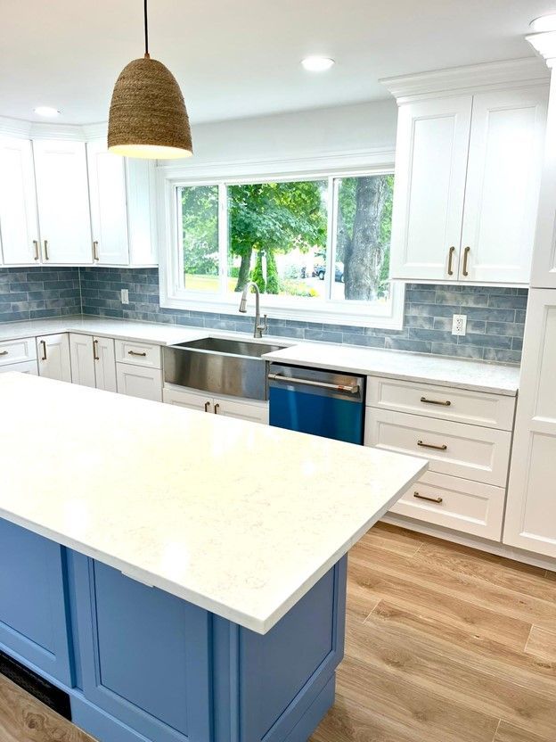 Modern kitchen with white cabinets, blue island, stainless steel sink, and wood floors.