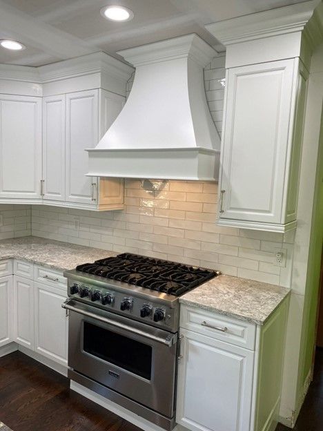 White kitchen with stainless steel range, white cabinets, and white range hood.