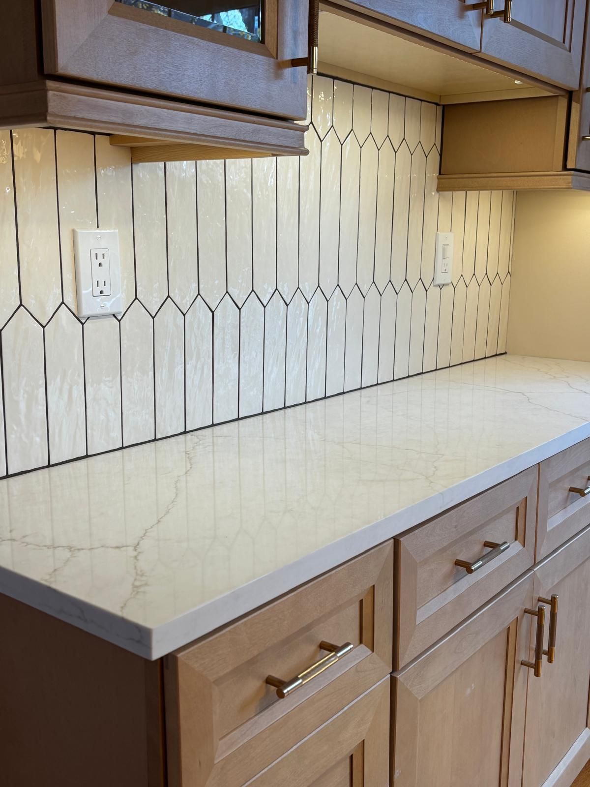Kitchen with light wood cabinets, white countertops, and patterned white backsplash.