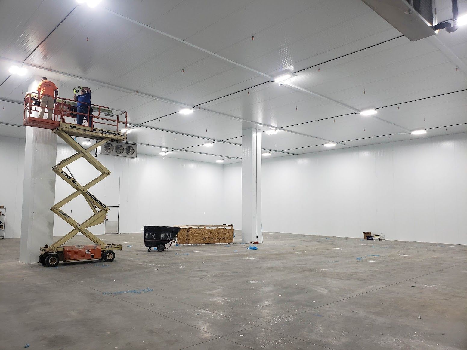A man is standing on a scissor lift in an empty warehouse.