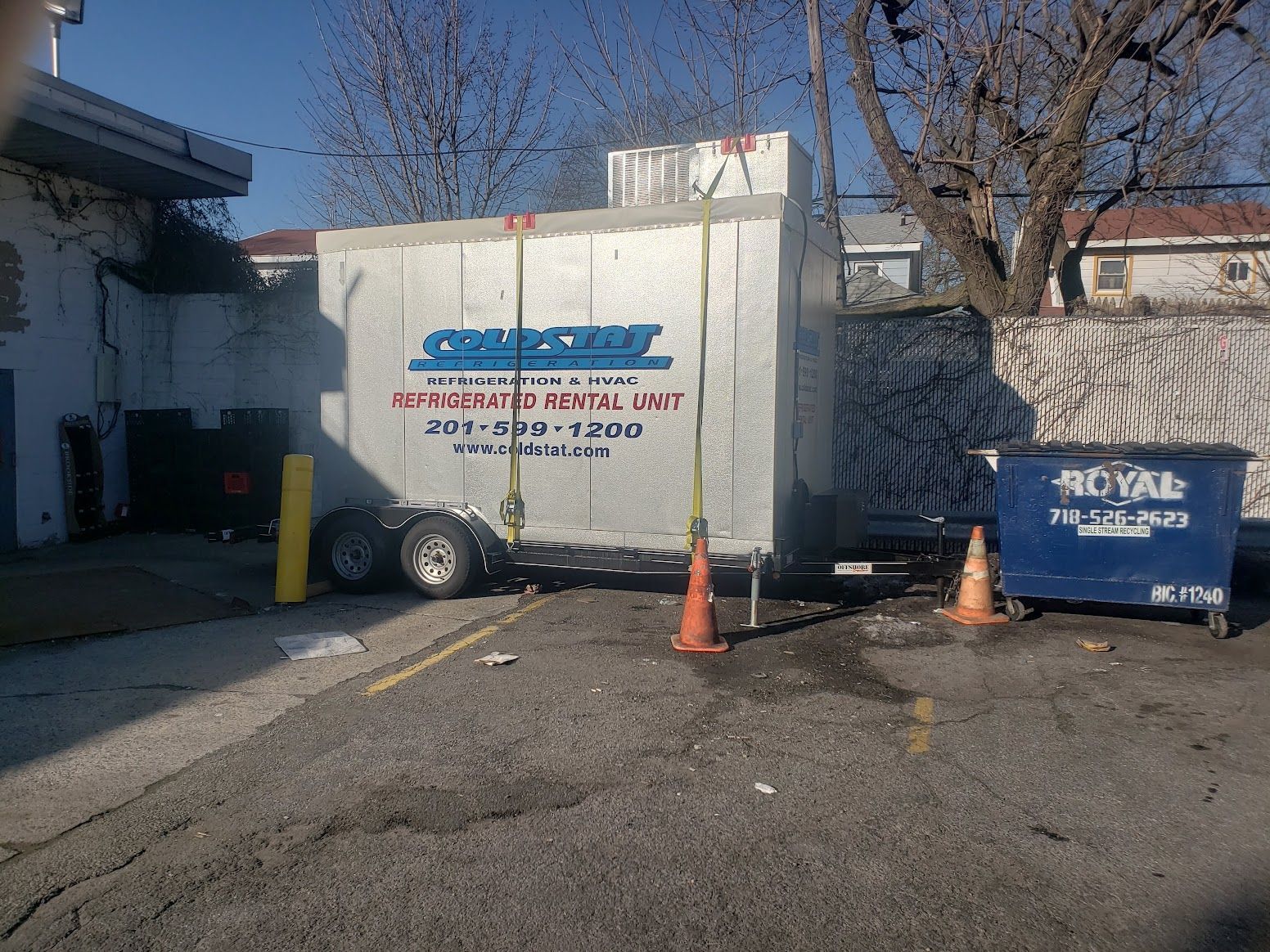 A white trailer is parked next to a blue dumpster that says royal