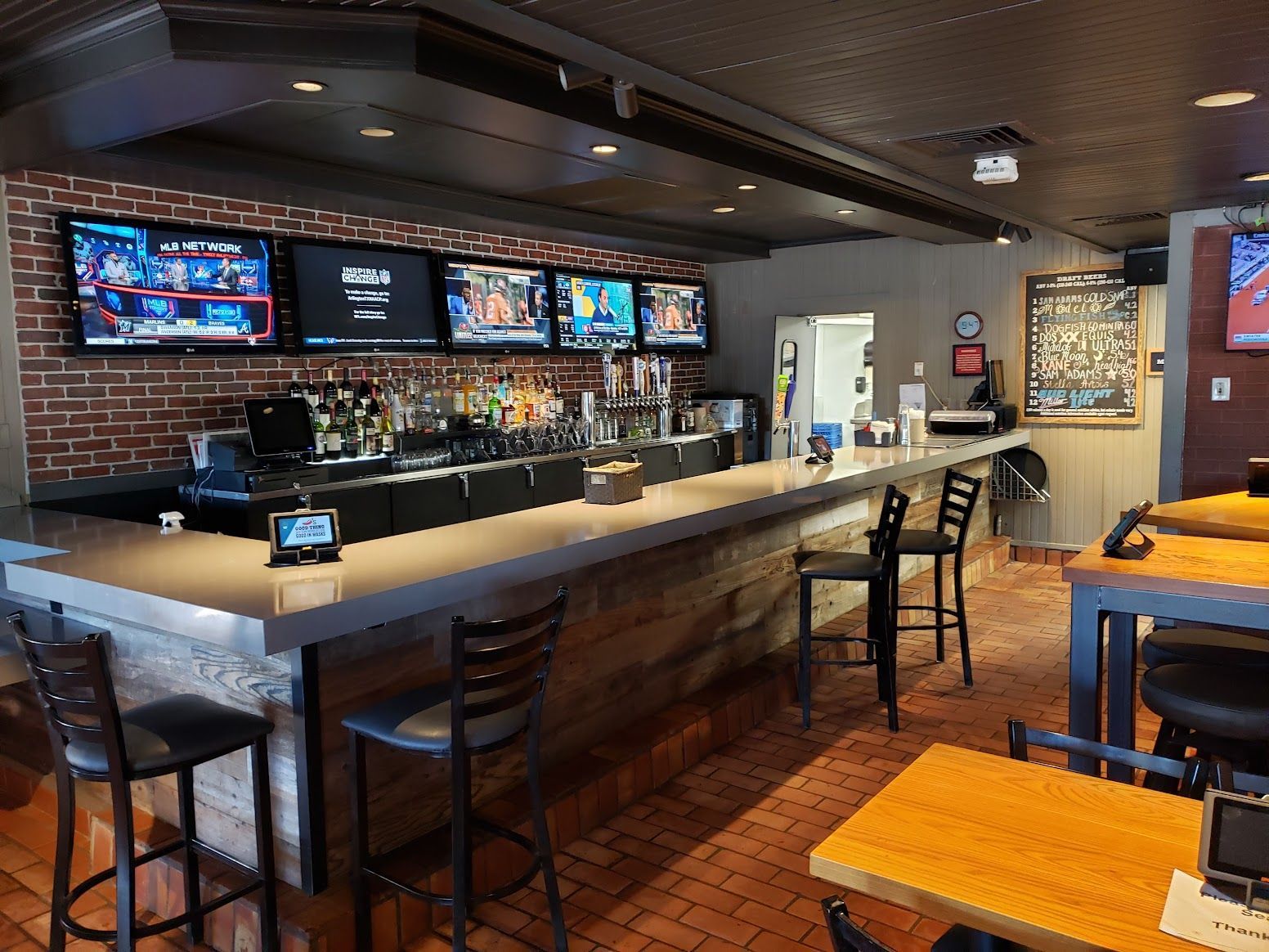 A bar in a restaurant with tables and chairs and televisions on the wall.
