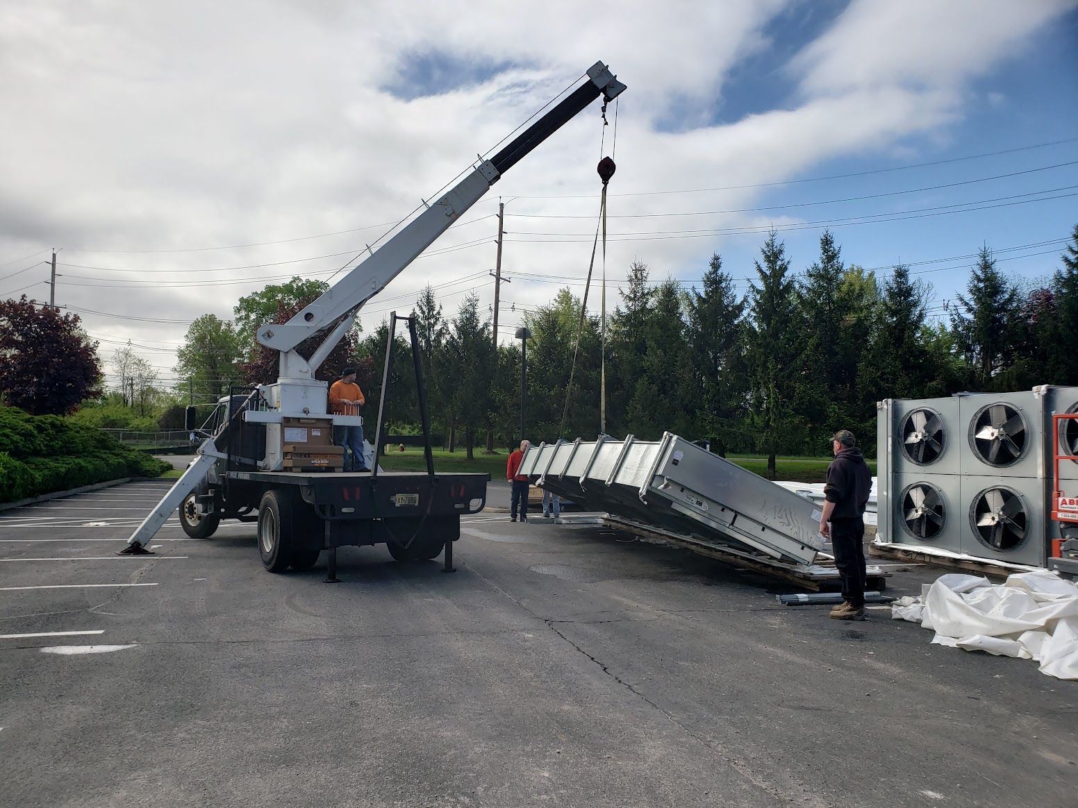 A crane is lifting a large piece of metal in a parking lot.