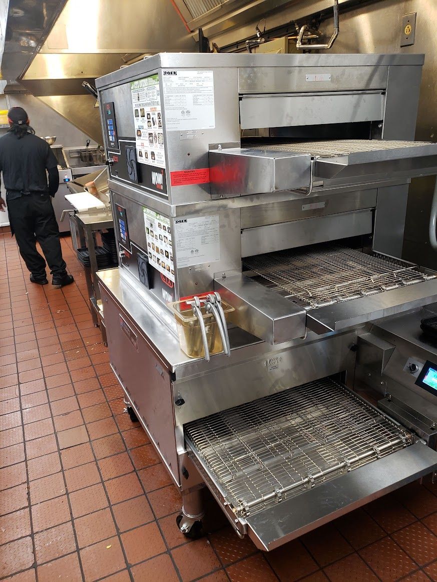 A man is standing in a kitchen next to a pizza oven.