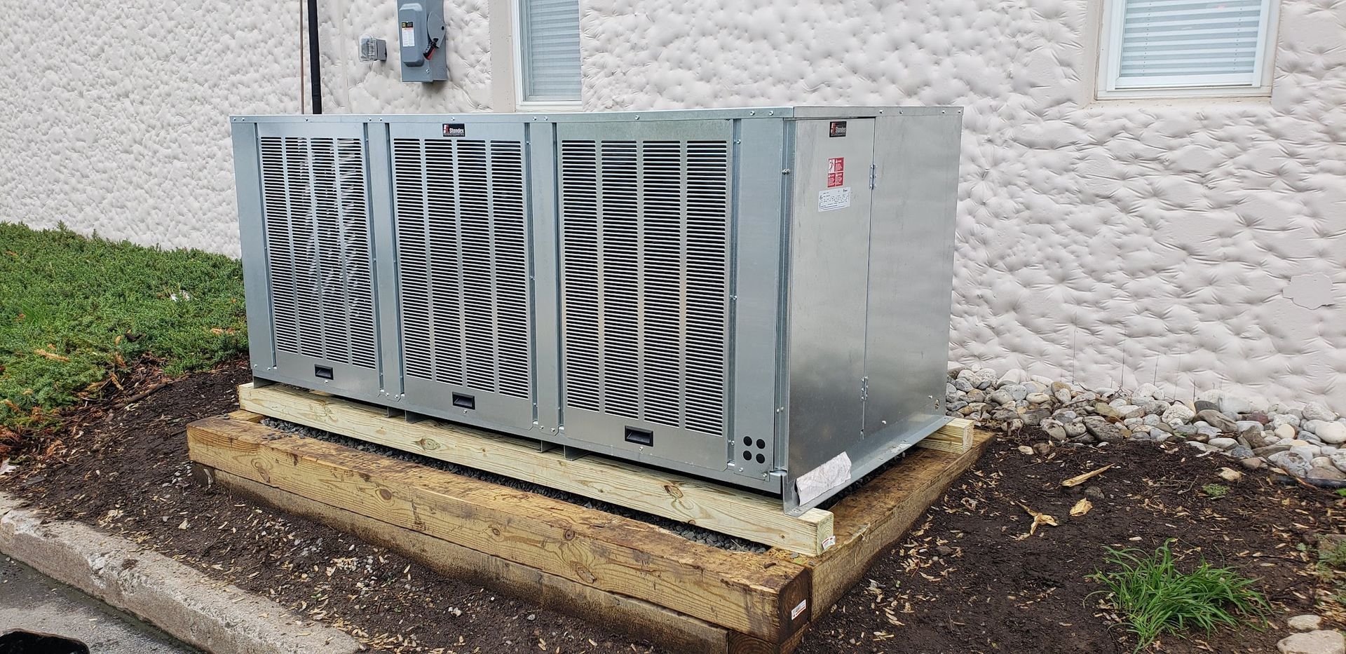 A large air conditioner is sitting on top of a wooden platform in front of a building.