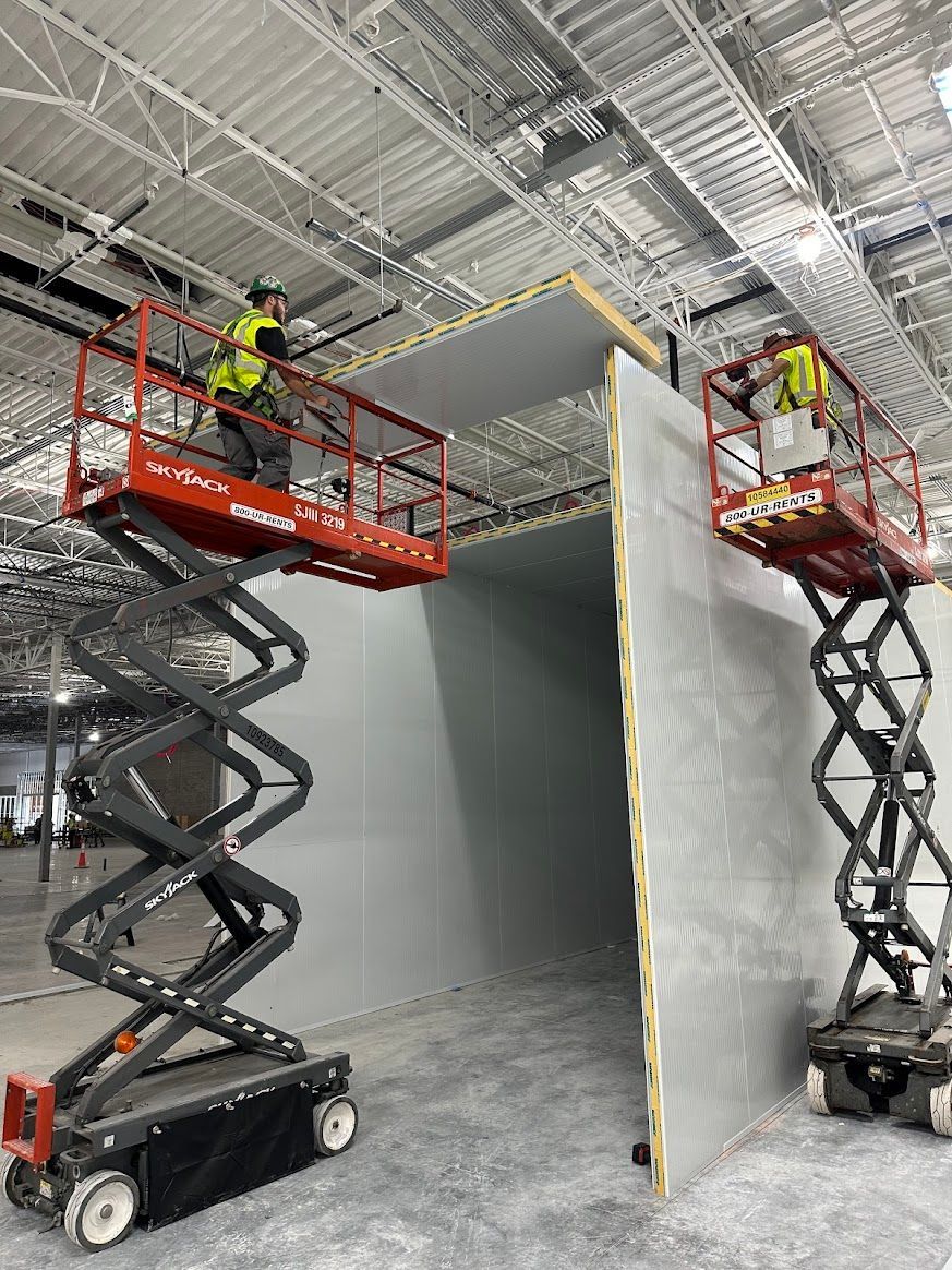 Two men are working on scissor lifts in a building.
