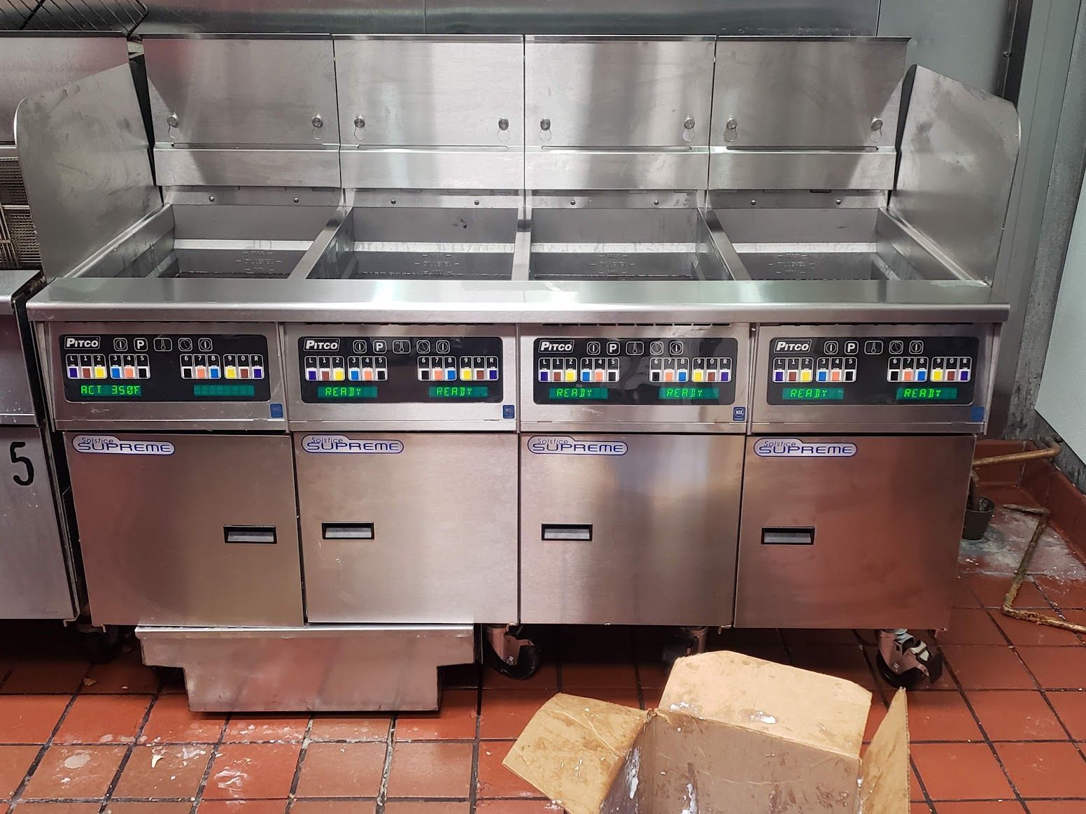 A stainless steel fryer is sitting on a tiled floor next to a box.