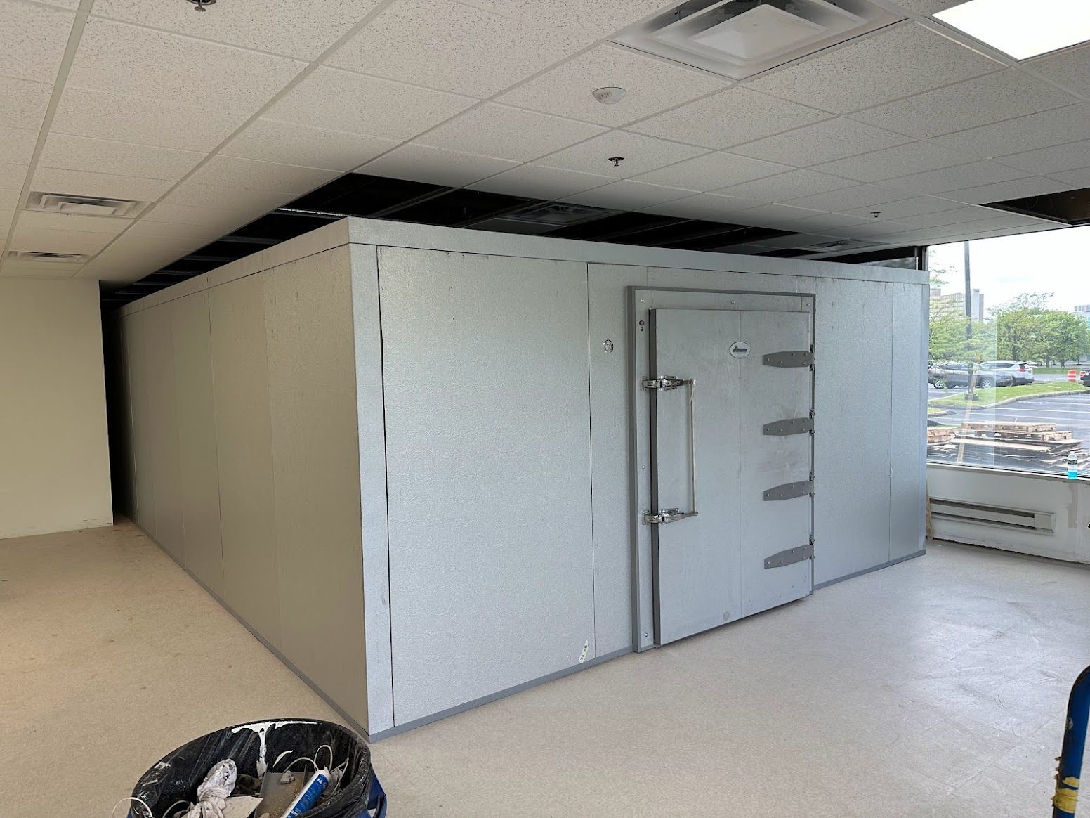 A large white room with a door and a trash can on the floor.