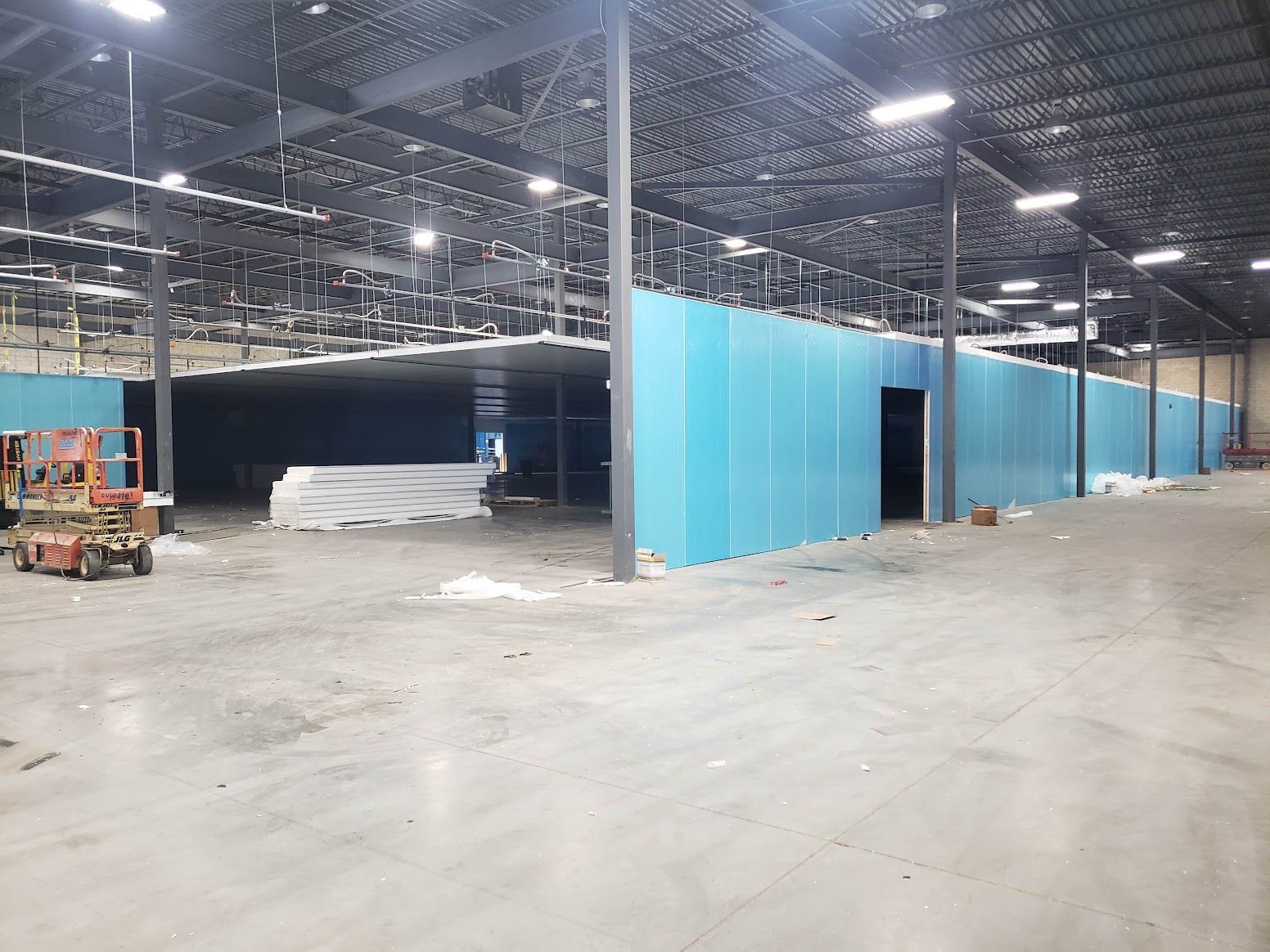 A large warehouse with blue walls and a forklift in the middle.
