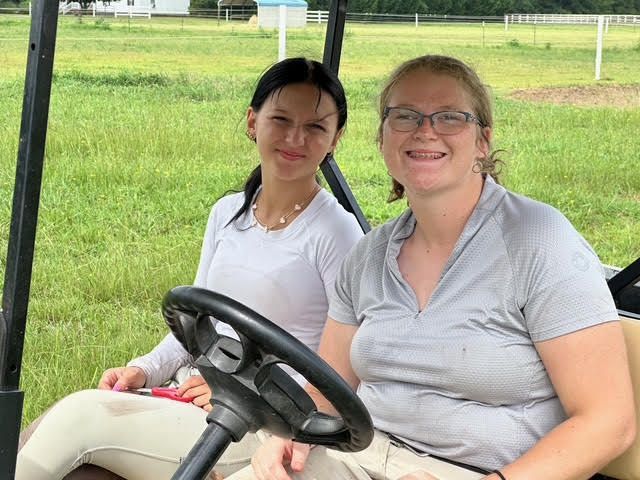 Two people smiling in a golf cart on a grassy field