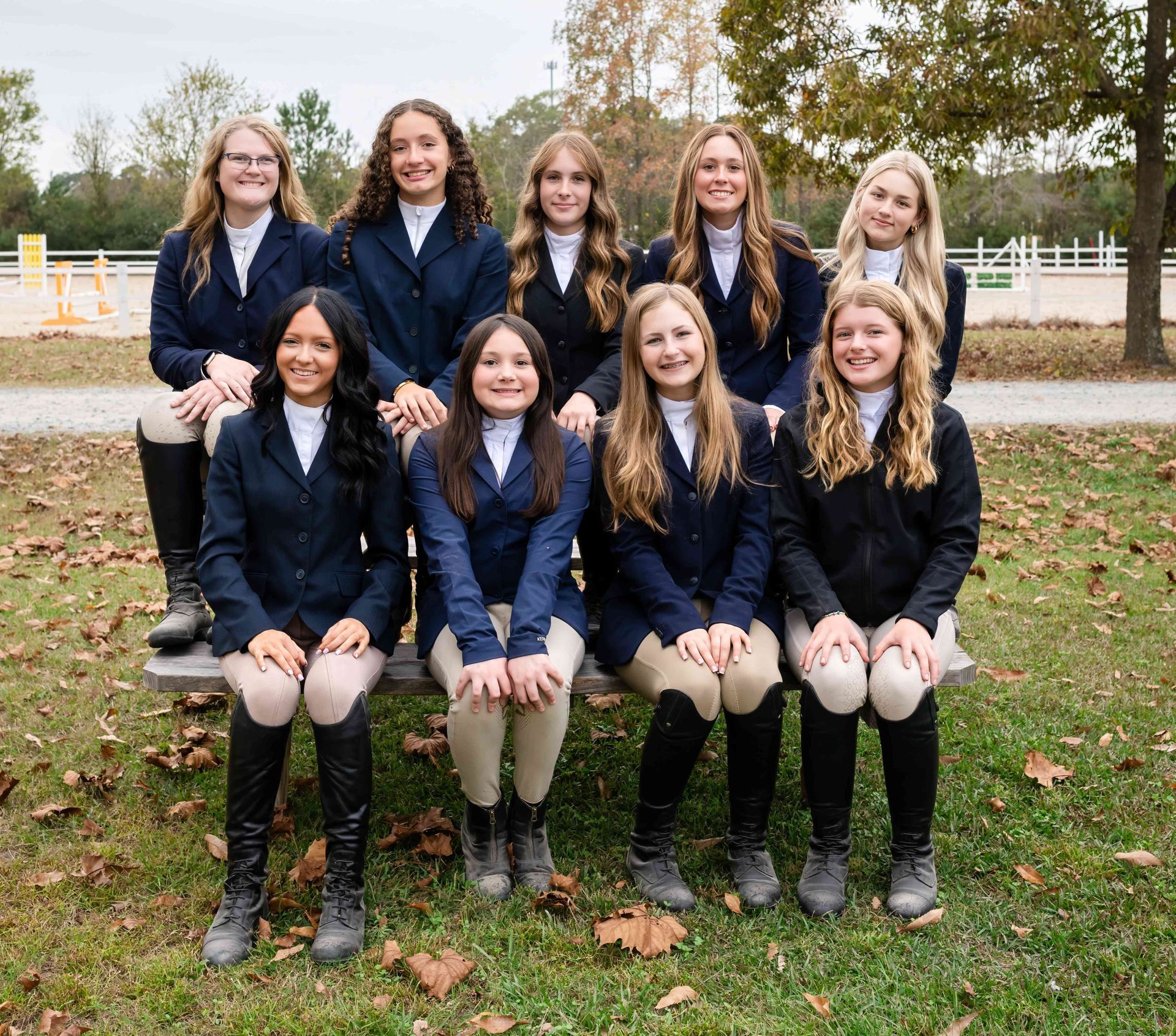 Nine people in navy blazers pose together outdoors on grass in autumn.