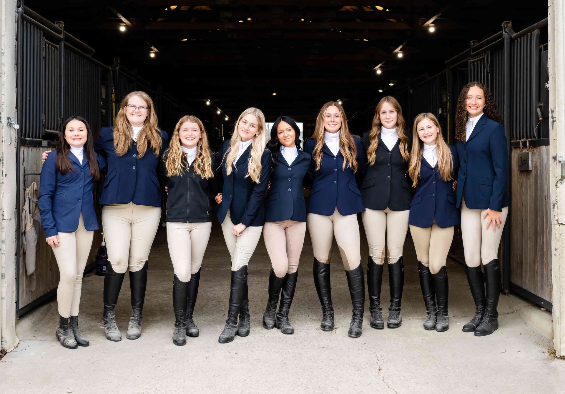 Group of ten people in navy blazers and khaki pants posing in a garage-like doorway
