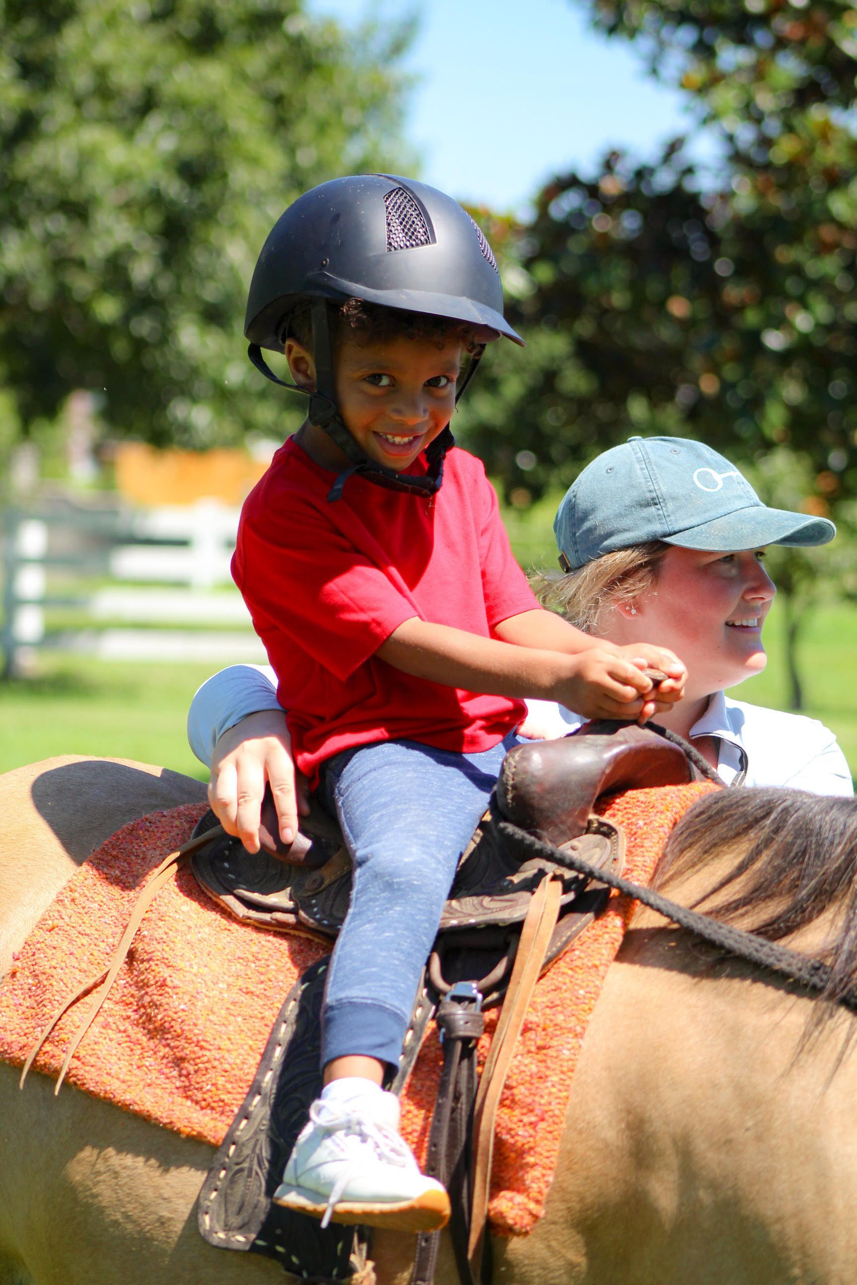 Child wearing a helmet riding a horse with an adult guiding from behind outdoors