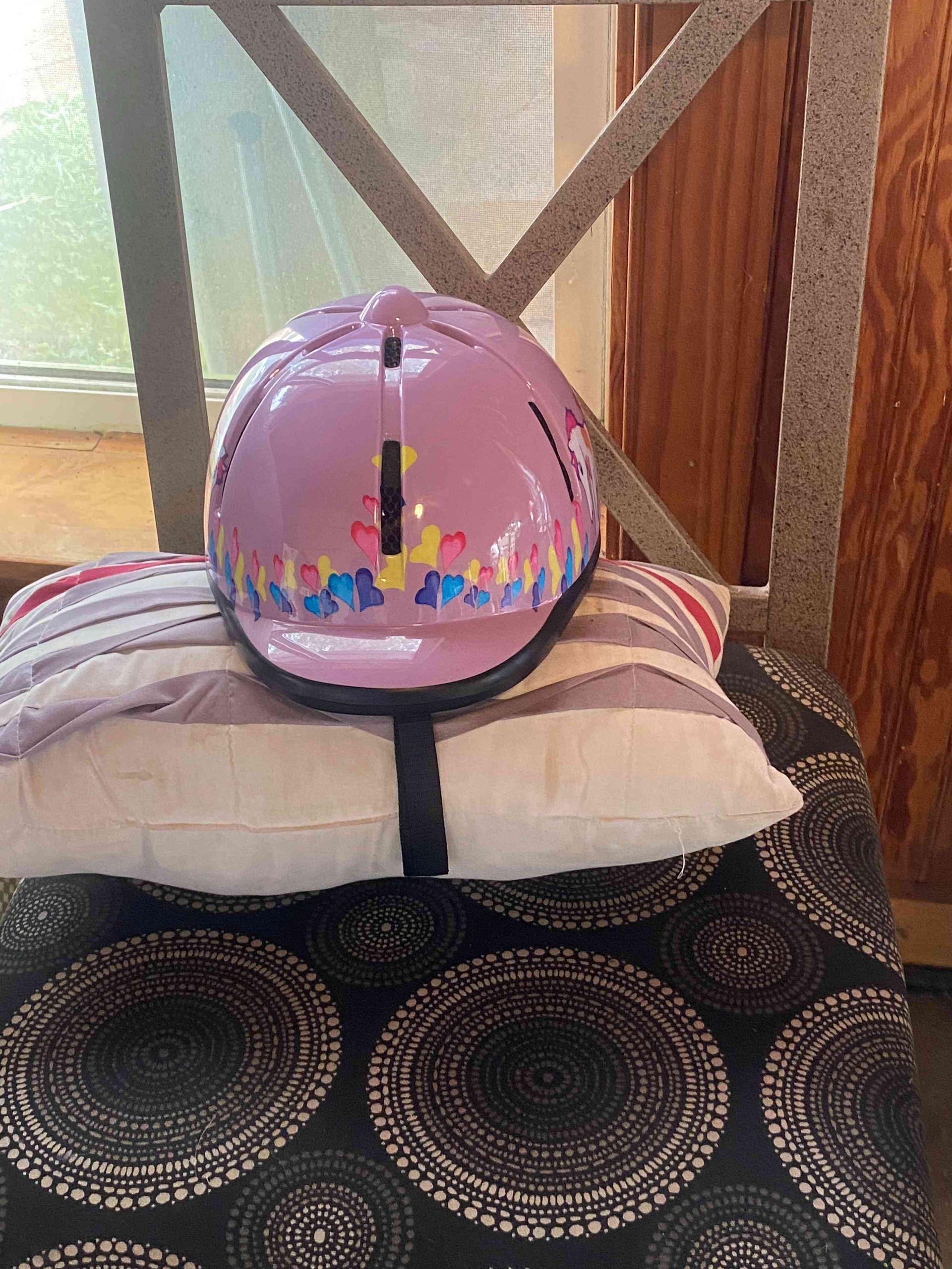 Pink helmet resting on stacked pillows on a patterned cushion by a window in a wooden room