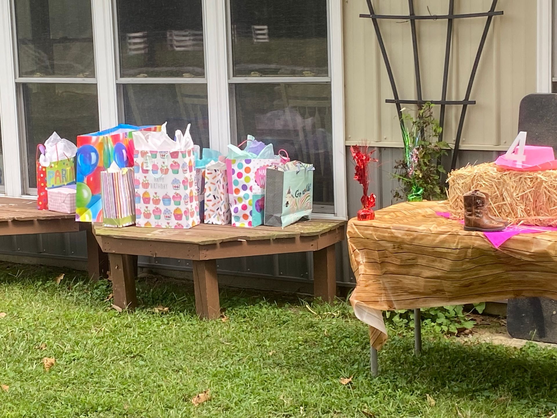 Gift bags on a wooden table and outdoor bench beside a window, with hay bale decorations in a yard