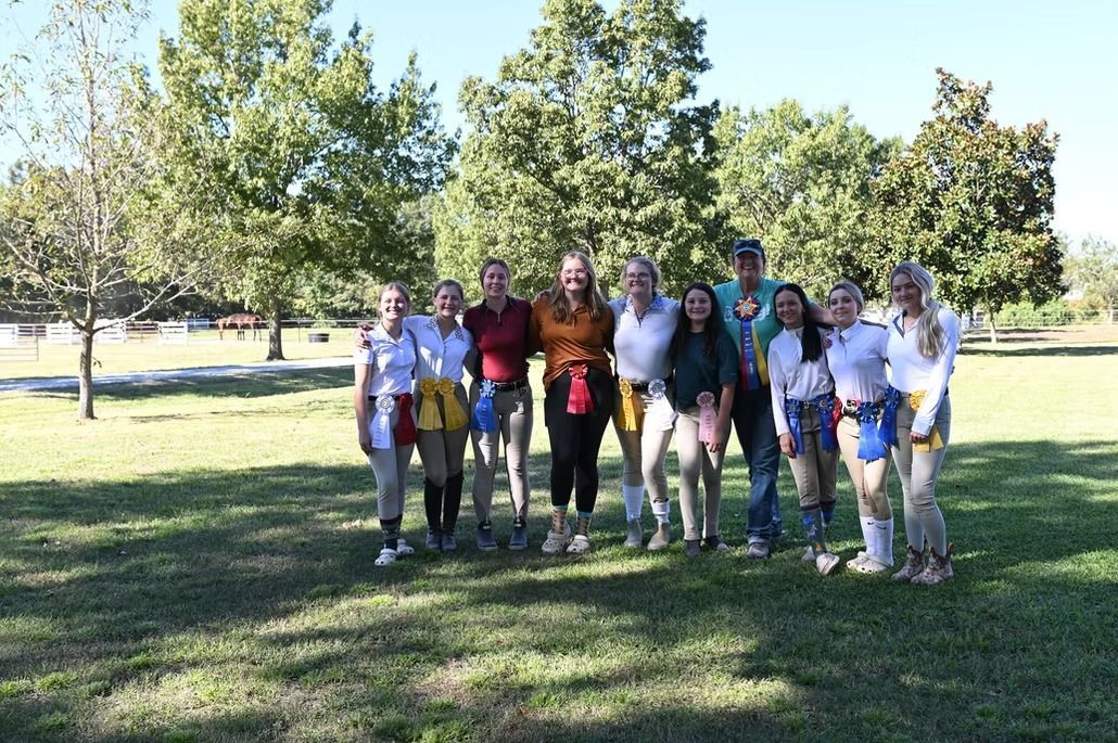Group of people standing together in a sunny park, posing on grass with trees in the background.