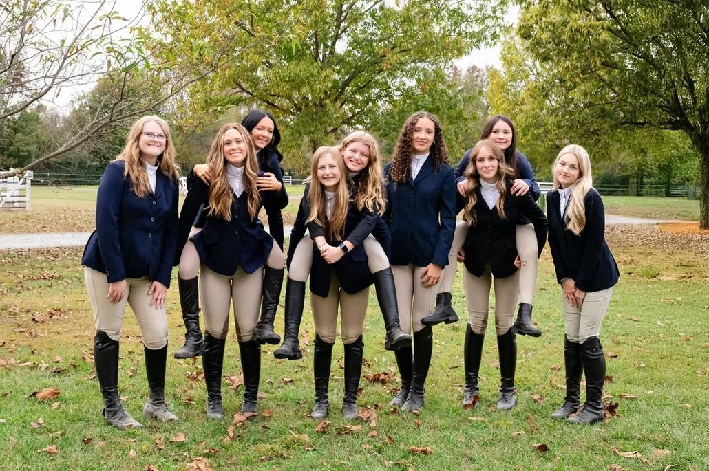 Eight people in navy outfits posing outdoors on a grassy field with trees in the background
