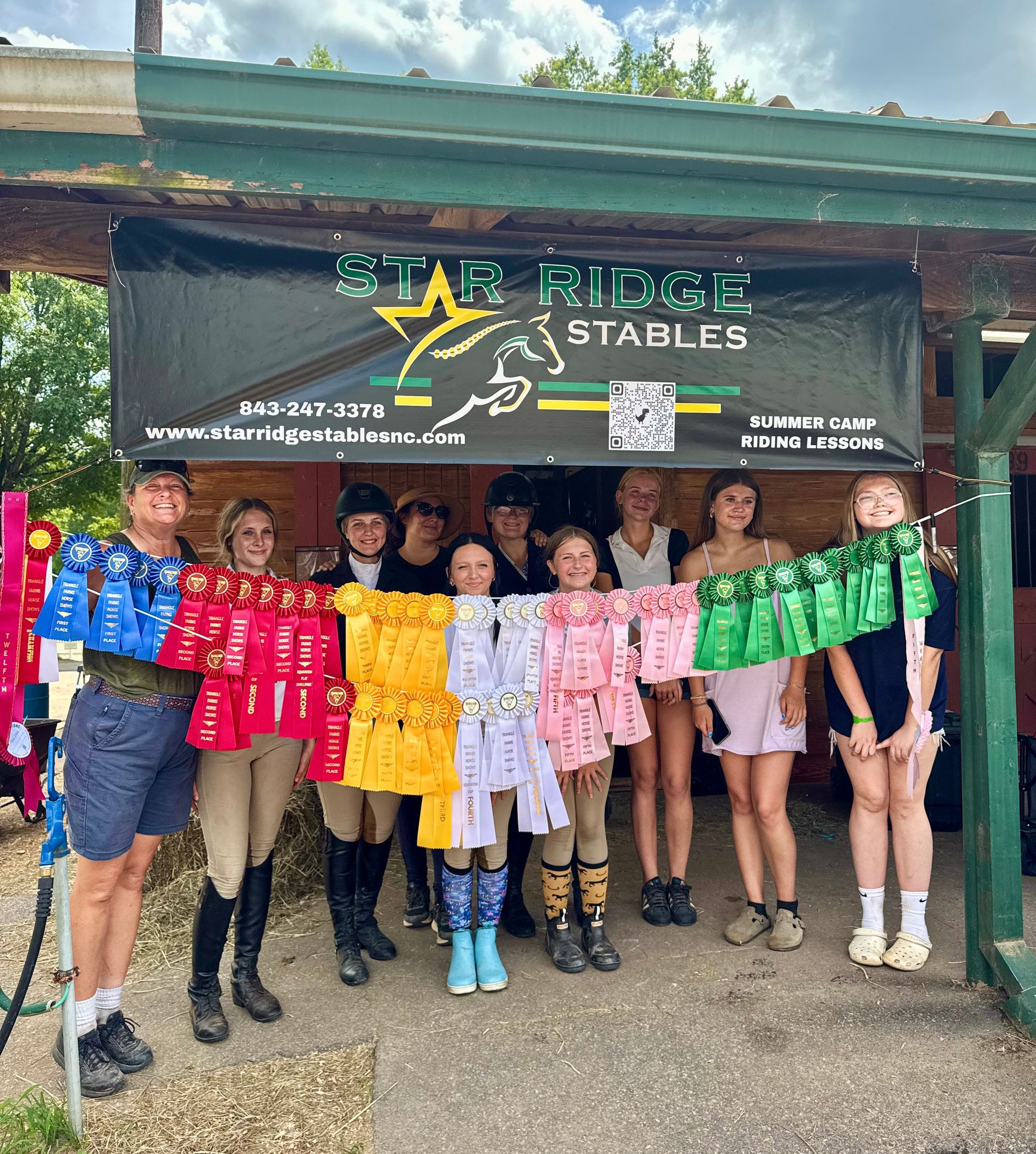 Group posing at Star Ridge Stables, holding a colorful rainbow banner in front of the barn.