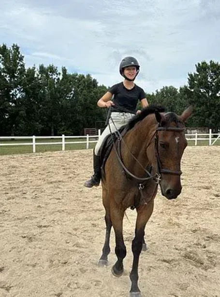 Rider in helmet on a brown horse in an outdoor riding arena.