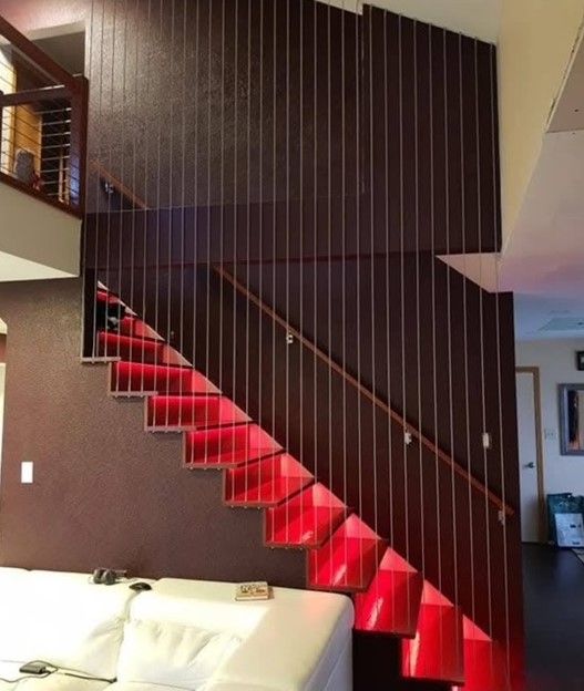 A staircase with red under-step lighting. Dark wood paneling and cable railing.