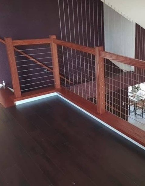 Wooden railing with wire mesh and vertical wires on a landing. Dark wood flooring and purple wall in the background.